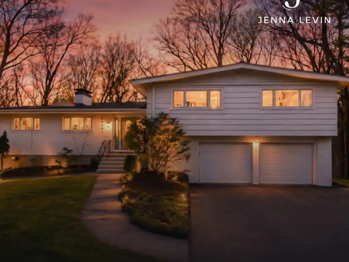 White split-level home with a double garage and glowing windows beneath a pink dusk sky.